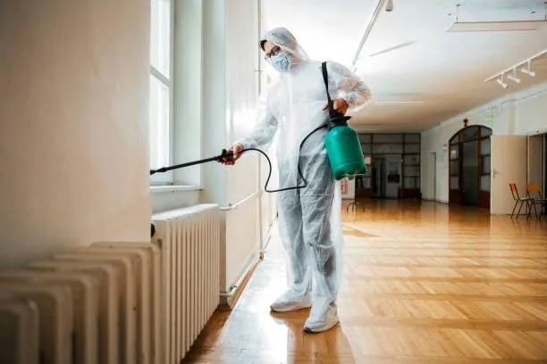 Technicien en combinaison de protection pulvérisant un insecticide à l'intérieur d'une maison créole en Guadeloupe